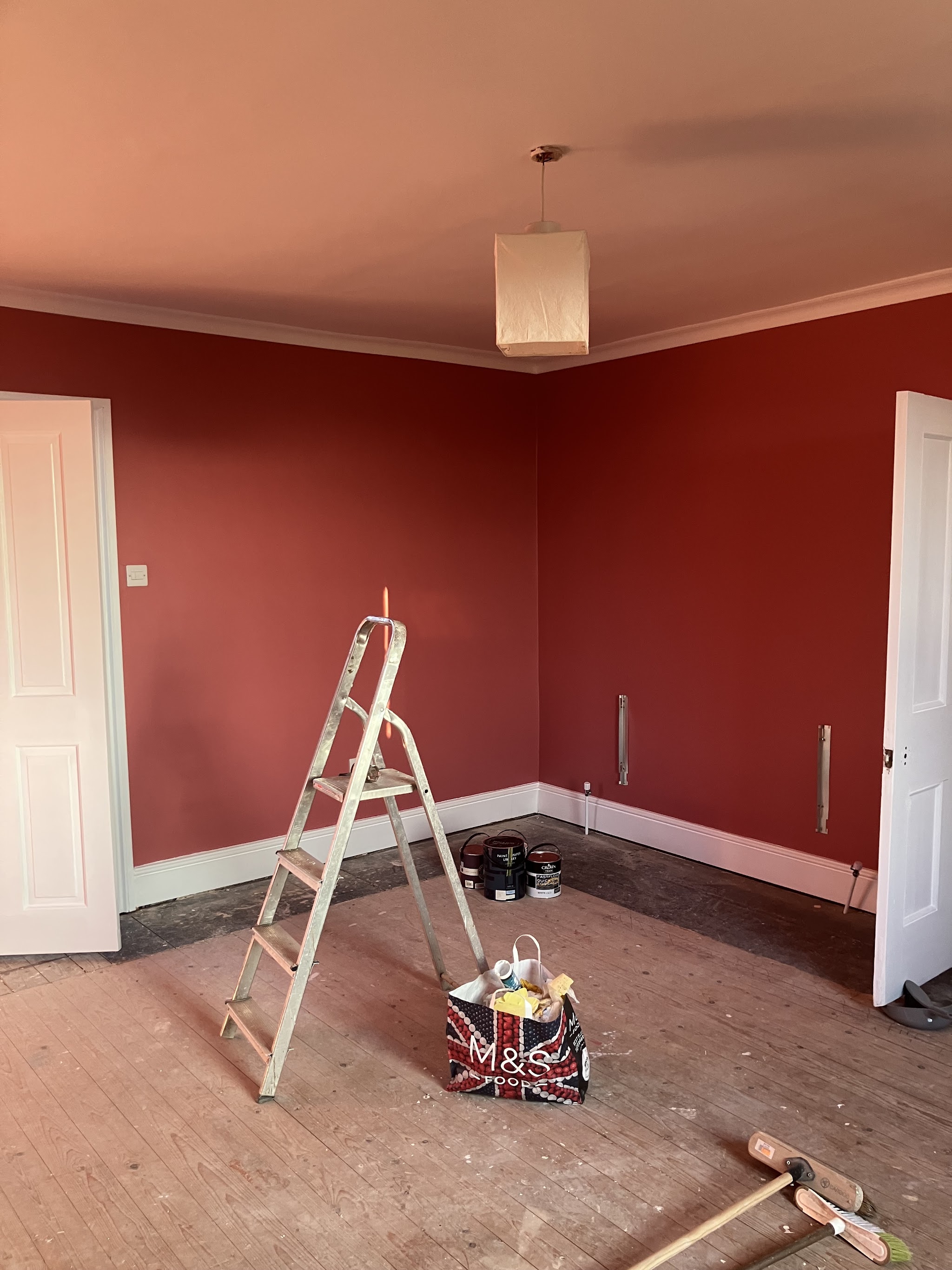 Bedroom freshly painted in a deep red with white skirting and a stepladder