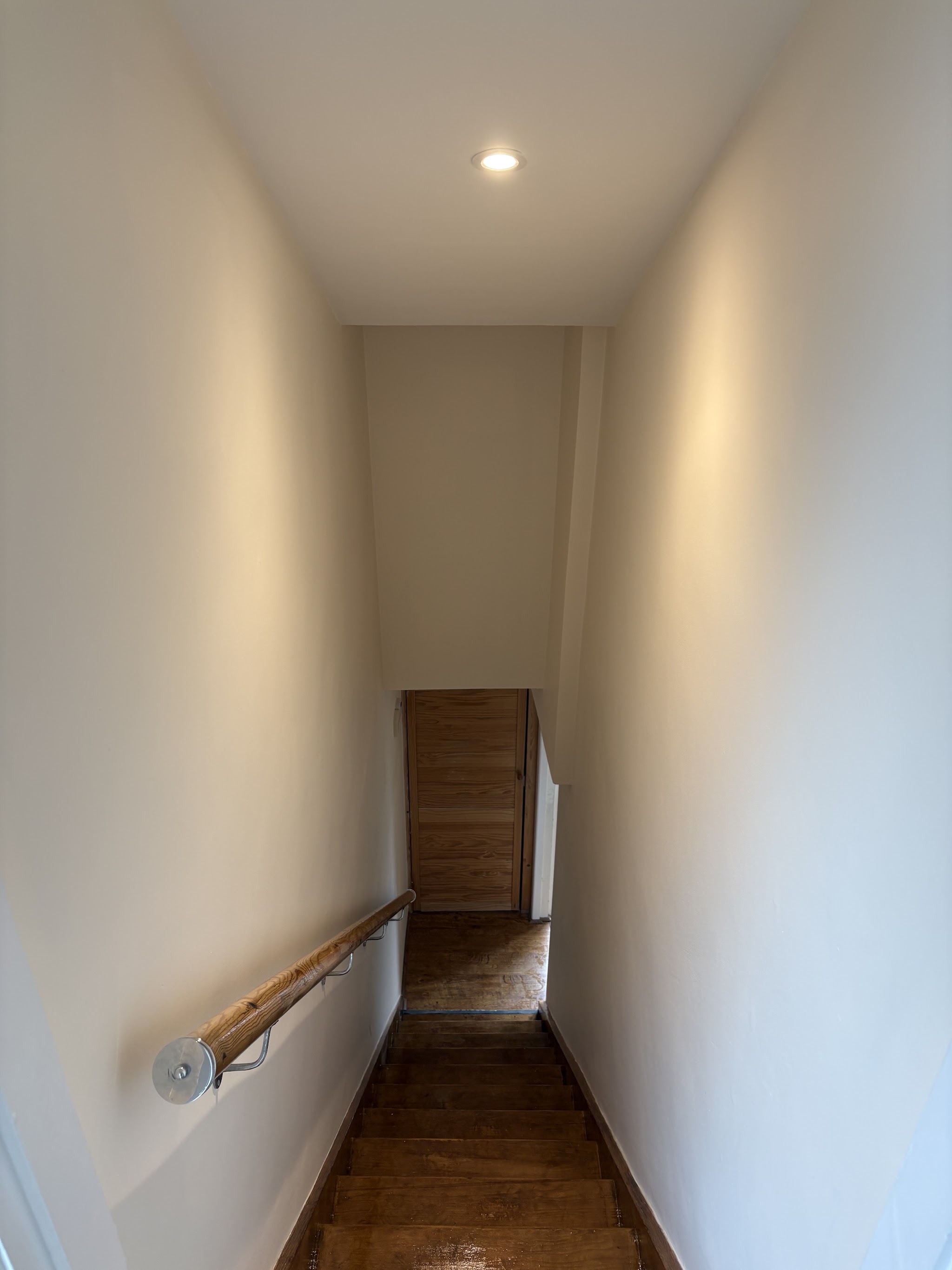 Finished narrow hallway and staircase in clean white with a wooden handrail